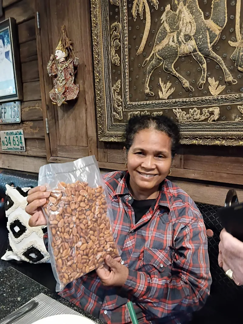 A woman smiling and holding up a clear bag of dried cacao beans in a wooden room